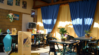 Acogedor comedor interior en Camping le Roc, Occitania, Francia, con cortinas azules y decoración colorida.