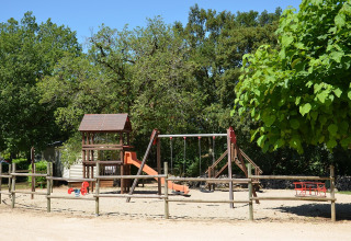 Parque infantil con columpios y tobogán en Camping le Roc, rodeado de árboles en Occitanie, Francia.