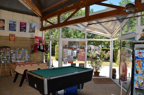 Sala de ocio en Camping le Roc con futbolín, billar y carteles, vista al jardín en Occitania, Francia.