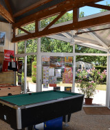 Sala de ocio en Camping le Roc con futbolín, billar y carteles, vista al jardín en Occitania, Francia.