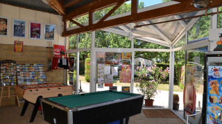 Sala de ocio en Camping le Roc con futbolín, billar y carteles, vista al jardín en Occitania, Francia.