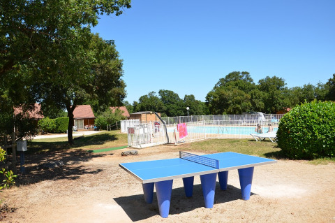 Mesa de ping-pong al aire libre junto a piscina vallada y bungalows en Camping le Roc, Occitanie, Francia.