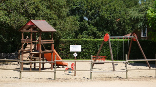 Parque infantil con juego de trepar, tobogán y columpios en Camping le Roc, Occitania, Francia, rodeado de árboles.