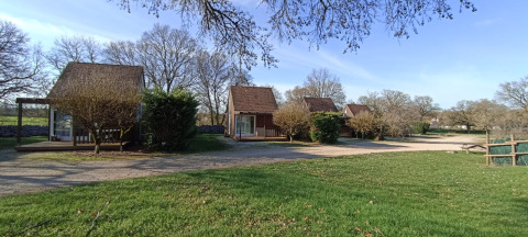 Charming wood cabins at Camping le Roc holiday park in Occitanie, France, surrounded by lawn and trees.