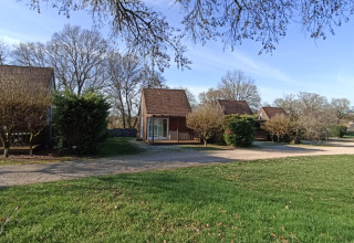 Houten huisjes op Camping le Roc in Occitanie, Frankrijk, omringd door groene bomen en open grasveld.