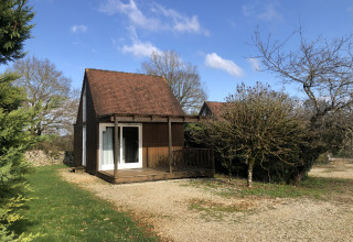 Een knus houten huisje met veranda bij Camping le Roc in Occitanie, Frankrijk, onder een blauwe lucht.