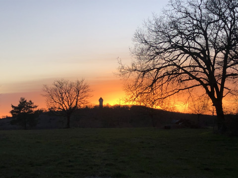 Atardecer en Camping le Roc, Occitanie, Francia, con siluetas de árboles y una torre de agua al fondo.