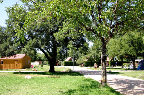 Camping le Roc en Occitania, Francia: parque vacacional con árboles, cabañas de madera y visitantes paseando.