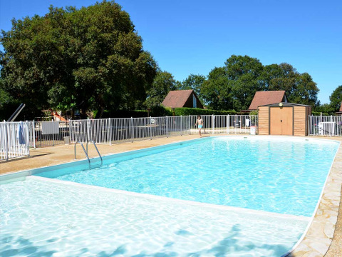 Piscina exterior rodeada de valla y árboles en Camping le Roc, un parque vacacional en Occitanie, Francia.