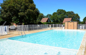 Udendørs swimmingpool omgivet af hegn og træer på Camping le Roc feriested i Occitanie, Frankrig.