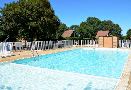 Outdoor swimming pool with safety fence and trees at Camping le Roc holiday park in Occitanie, France.