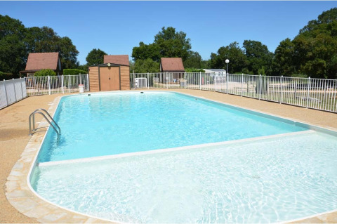 Piscina al aire libre en Camping le Roc, Occitania, Francia, rodeada de vallas y casas de madera.