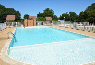 Piscina all'aperto al Camping le Roc in Occitania, Francia, circondata da recinzioni e alberi verdi.