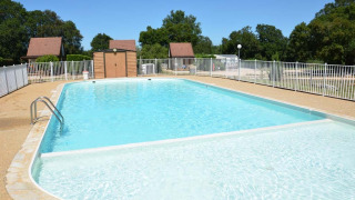 Piscina al aire libre en Camping le Roc, Occitania, Francia, rodeada de vallas y casas de madera.