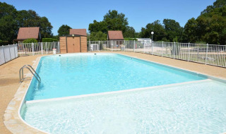 Piscina al aire libre en Camping le Roc, Occitania, Francia, rodeada de vallas y casas de madera.