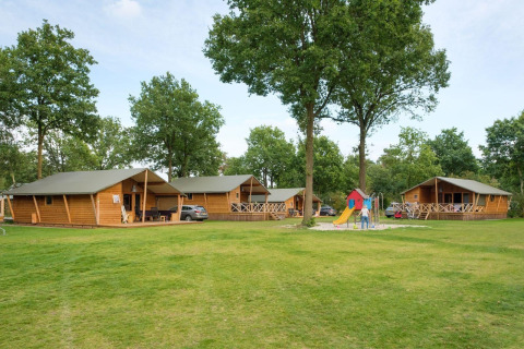 Rheezerlodge DeLuxe low en Kampeerdorp de Zandstuve, Países Bajos, con cabañas, parque infantil y árboles.