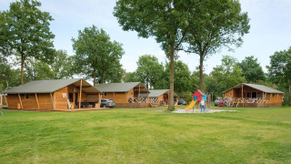 Rheezerlodge DeLuxe low en Kampeerdorp de Zandstuve, Países Bajos, con cabañas, parque infantil y árboles.