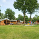 Rheezerlodge DeLuxe lavt ved Kampeerdorp de Zandstuve i Holland med hytter, legeplads og grønne træer.