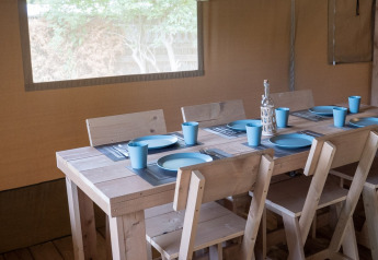 Interior de una tienda safari con mesa de madera, seis sillas y vajilla azul, lista para una comida.