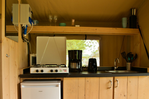 Small kitchen area inside a safari tent with gas stove, coffee maker, toaster, sink, and fridge.