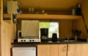 Kleine keuken in een safaritent met gasfornuis, koffiezetapparaat, broodrooster, gootsteen en koelkast.