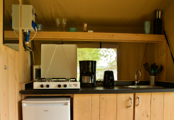 Small kitchen area inside a safari tent with gas stove, coffee maker, toaster, sink, and fridge.