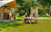 Familie entspannt an einem Safarizelt mit Spielplatz im Grünen auf dem Campingplatz Sevink Molen.