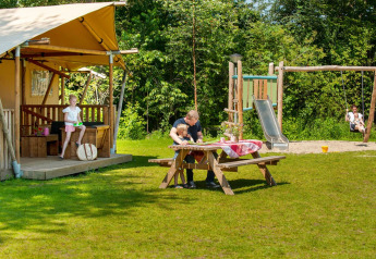 Famiglia si gode attività all’aperto vicino a una tenda safari con parco giochi al Camping Sevink Molen.