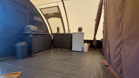 Binnenzijde van een tunneltent bij Camping Sevink Molen, met keuken, koelkast en vuilnisbak te zien.