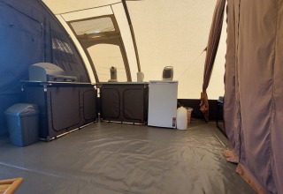 Intérieur d'une tente tunnel au Camping Sevink Molen, avec cuisine, réfrigérateur et poubelle visibles.