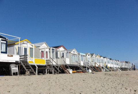 Colorful beach cabins on the sand at Welcome.in holiday park, Dishoek, Zeeland, Netherlands under blue sky.