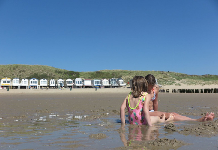 Two children play in sand and water near colorful beach huts at Welcome.in - Zeeland - Dishoek holiday park, Netherlands.