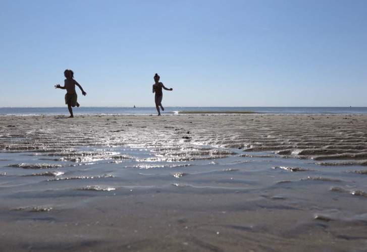 Zwei Kinder rennen und spielen am flachen Sandstrand bei sonnigem Wetter in Zeeland, Niederlande.