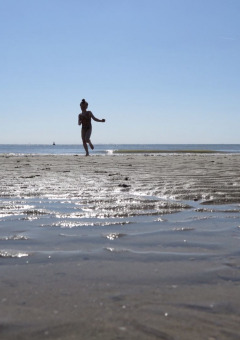 Dos niños corren y juegan en una playa arenosa con marea baja bajo un cielo azul claro en Zeeland, Países Bajos.