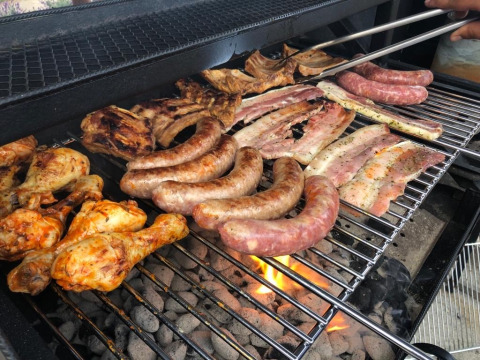 Barbecue with sausages, chicken drumsticks, and ribs grilling at Camping De La Vallée, Belgium.