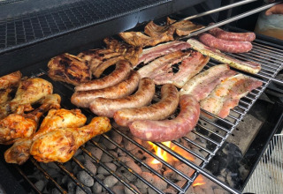 Barbecue with sausages, chicken drumsticks, and ribs grilling at Camping De La Vallée, Belgium.