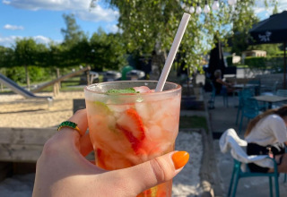 Hand holds a summer drink with strawberries and ice at Camping De La Vallée, Luxembourg, Belgium, outdoors.