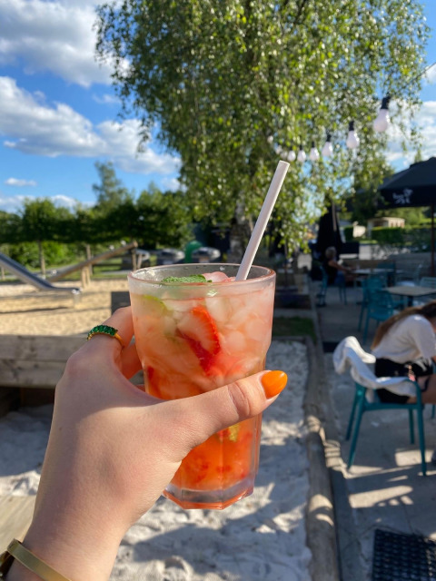 Mano sostiene bebida veraniega con fresas y hielo en Camping De La Vallée, Luxemburgo, Bélgica, al aire libre.