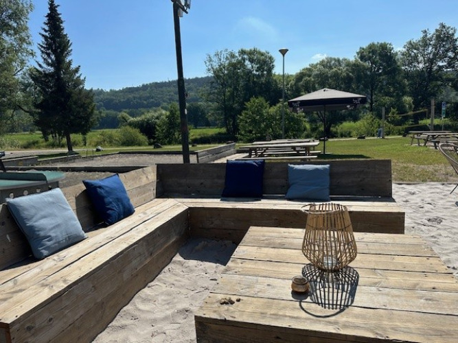 Outdoor seating area with wooden benches and cushions at Camping De La Vallée in Belgian Luxembourg.