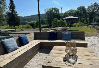 Outdoor seating area with wooden benches and cushions at Camping De La Vallée in Belgian Luxembourg.