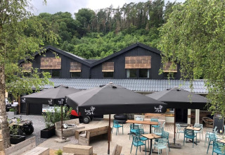 Outdoor café area at Camping De La Vallée in Belgium, surrounded by greenery and a modern lodge building.