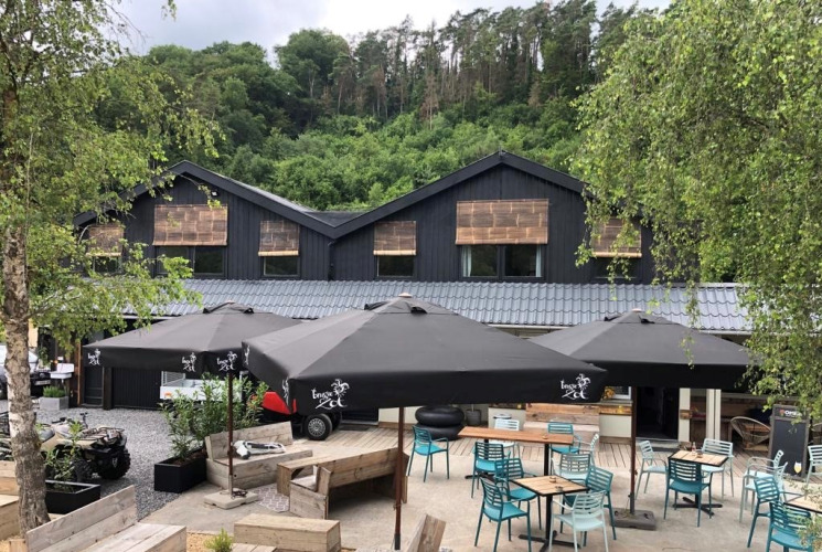 Outdoor café area at Camping De La Vallée in Belgium, surrounded by greenery and a modern lodge building.