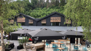 Außencafébereich im Camping De La Vallée in Belgien, umgeben von Bäumen und moderner Architektur.