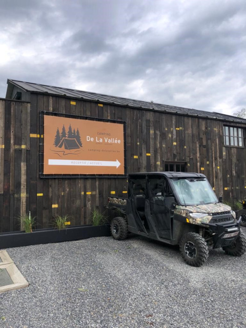 Camping De La Vallée sign and off-road vehicle in front of a wooden building at a holiday park in Belgium.
