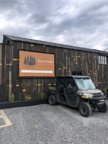 Camping De La Vallée sign and off-road vehicle in front of a wooden building at a holiday park in Belgium.