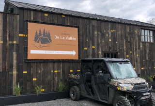 Cartel de Camping De La Vallée y vehículo todoterreno frente a edificio en parque vacacional de Bélgica.