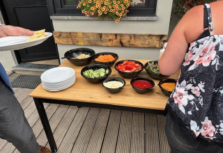 Mesa buffet al aire libre con varios vegetales e ingredientes de ensalada en Camping De La Vallée en Bélgica.