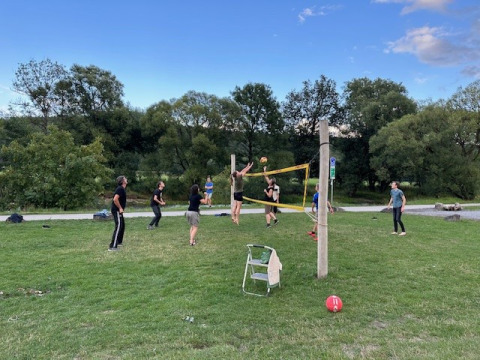 Folk spiller volleyball på en græsplæne under blå himmel i Camping De La Vallée, Belgien.