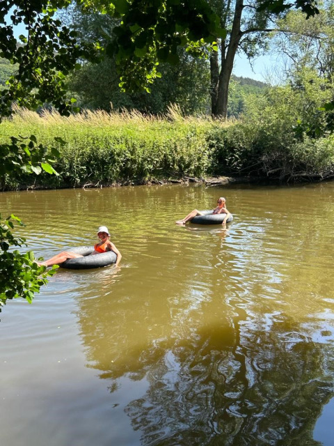 Due persone si rilassano su ciambelle gonfiabili che galleggiano in un fiume tranquillo circondato dal verde.