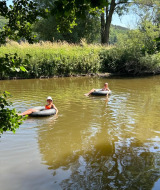 Dos personas se relajan en flotadores inflables sobre un río tranquilo rodeado de vegetación y árboles.